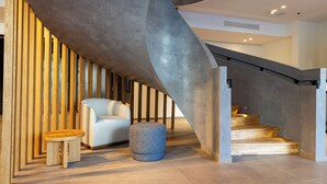 Un interior moderno con techo curvo, una escalera, un sillón azul claro y un otoman redondo.