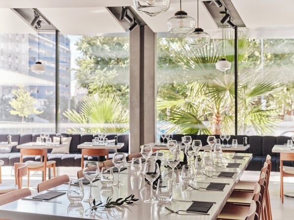Un restaurant avec une longue table à manger, dressée avec des verres à vin et des couverts, entourée de chaises et d’un canapé.