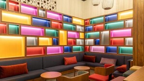 A modern lounge area with a sectional sofa, round tables, and colorful illuminated panels on the walls. - Wink Hotel Danang Riverside (Da Nang)