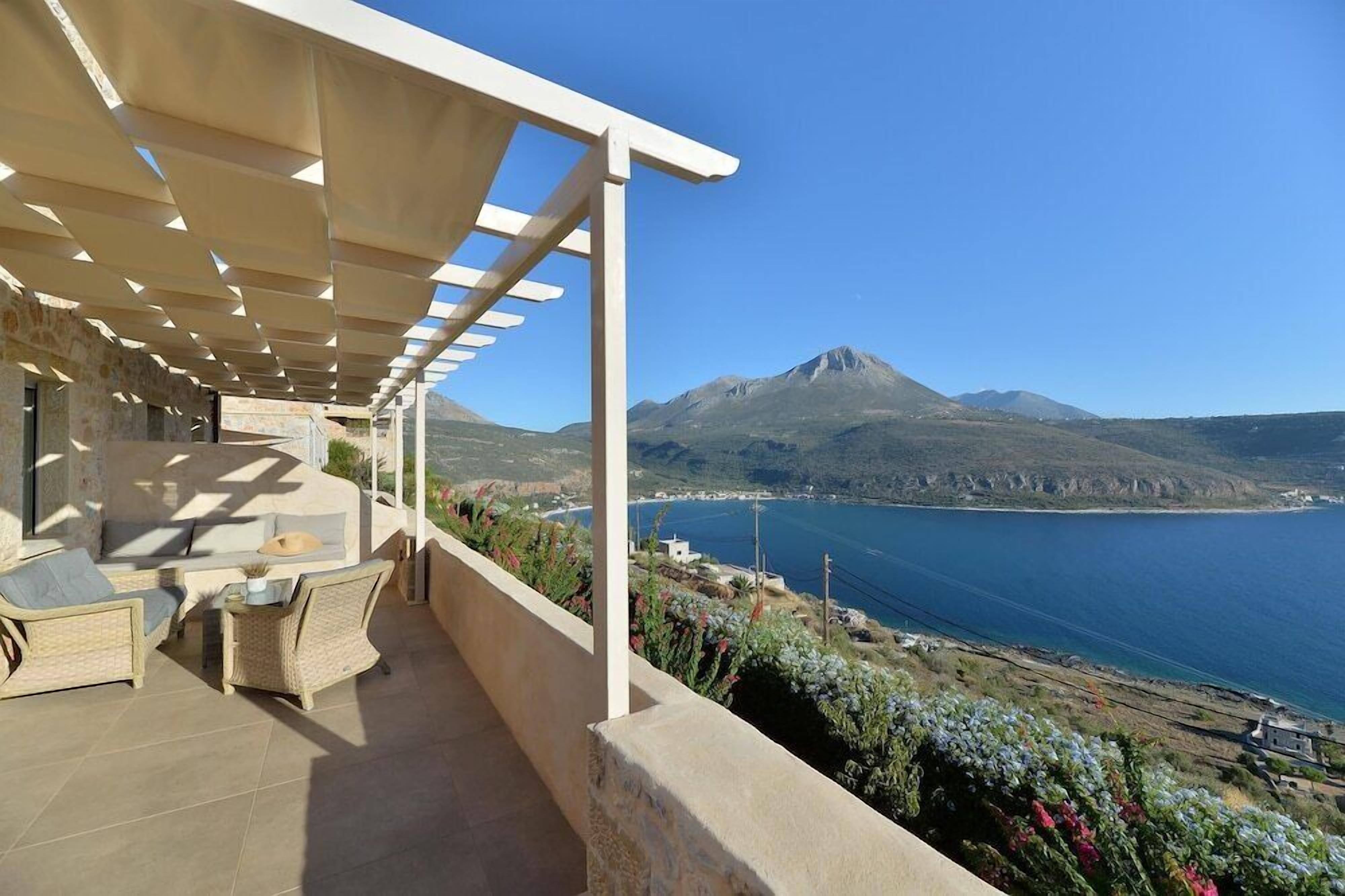 A balcony with outdoor furniture, a pergola, and a view of a mountain and sea.