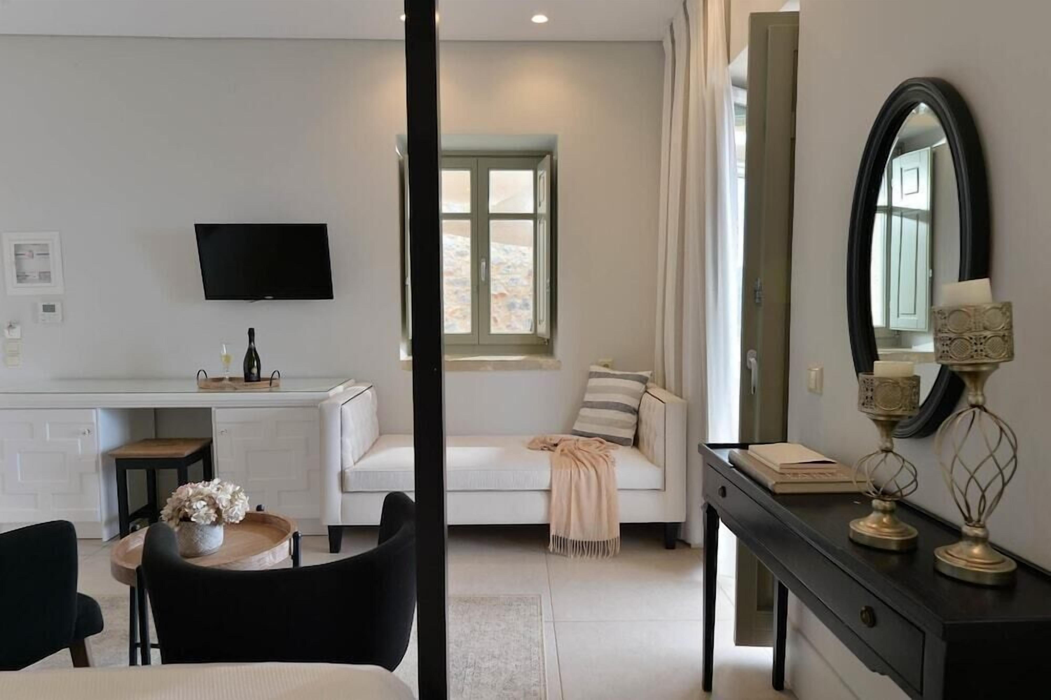 Una habitación moderna con televisión de pantalla plana, un sofá, una mesa de comedor con sillas, un escritorio y un espejo grande.