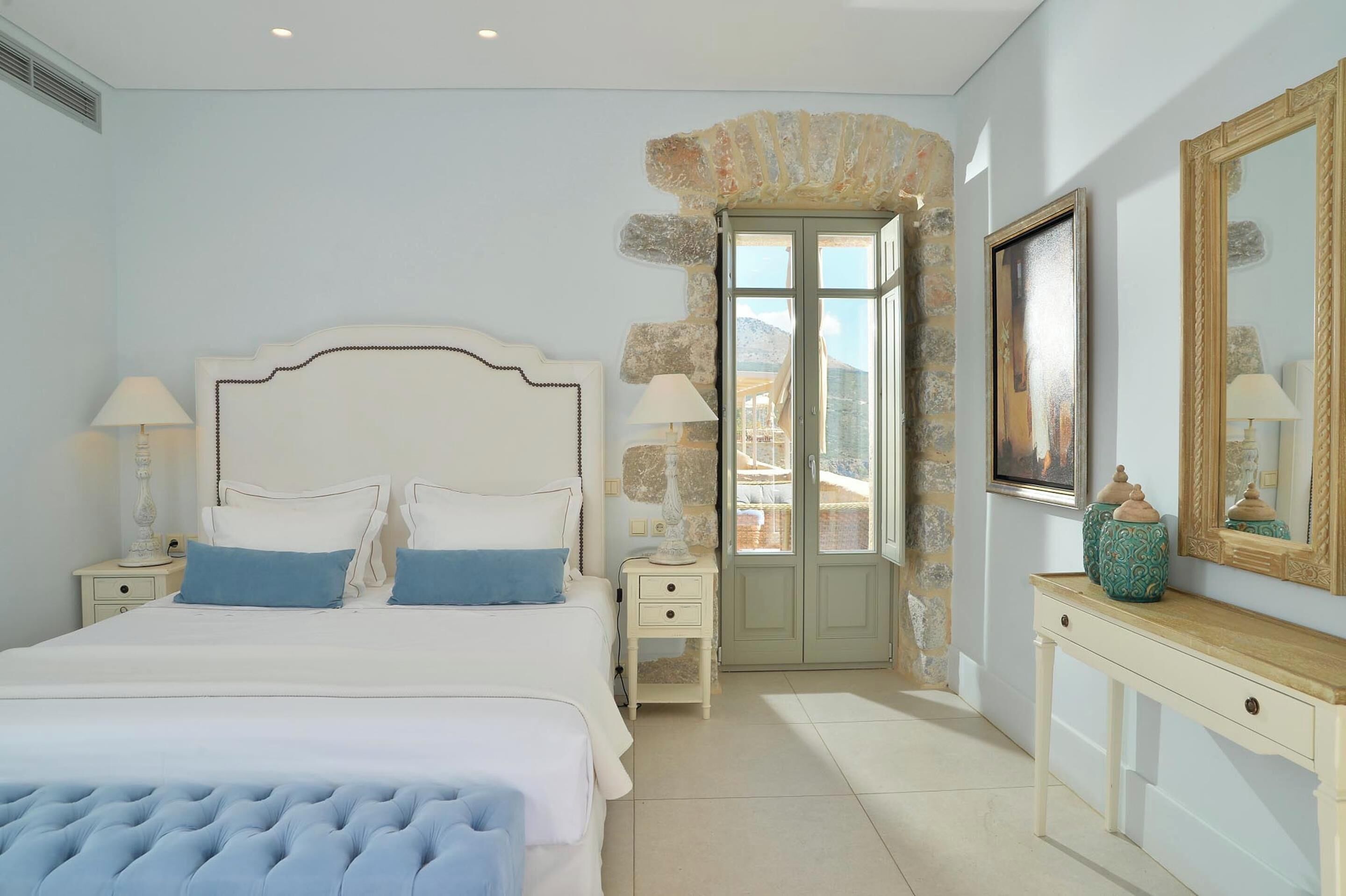 Un dormitorio con una cama grande, una pared de piedra, una puerta a un balcón y una mesita de consola con adornos.