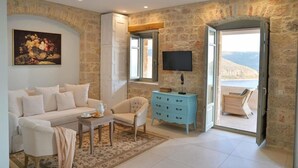 Una sala de estar con sofá, sillón, mesa de centro y televisor. Se observa una pared de piedra y una puerta que da al exterior.