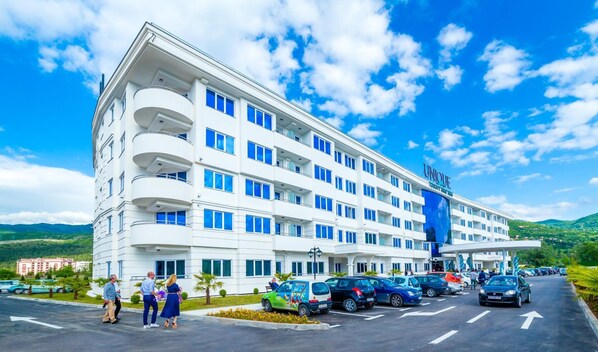 A multi-story hotel with a white facade, multiple balconies, and a parking lot with several cars. - Unique Resort & Spa (Ohrid)