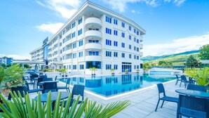 A modern hotel with a large pool, outdoor seating, and a scenic view of hills. - Unique Resort & Spa (Ohrid)