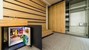 A compact room with a built-in mini-fridge stocked with beverages, a wooden slatted wall, and a walk-in closet with shelves and drawers. - Unique Resort & Spa (Ohrid)