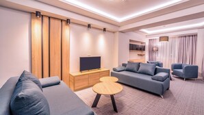A modern living room with a sofa set, a TV on a wooden cabinet, and a round coffee table. - Unique Resort & Spa (Ohrid)