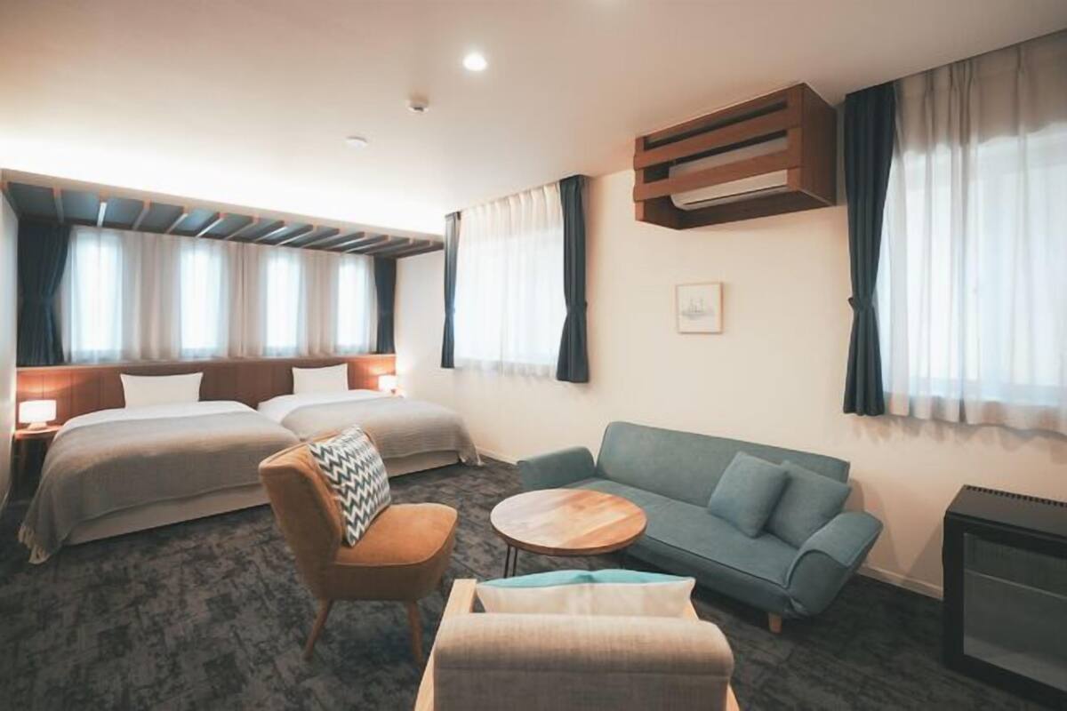Une chambre d’hôtel avec deux lits, un canapé, un fauteuil, une petite table et une cheminée.
