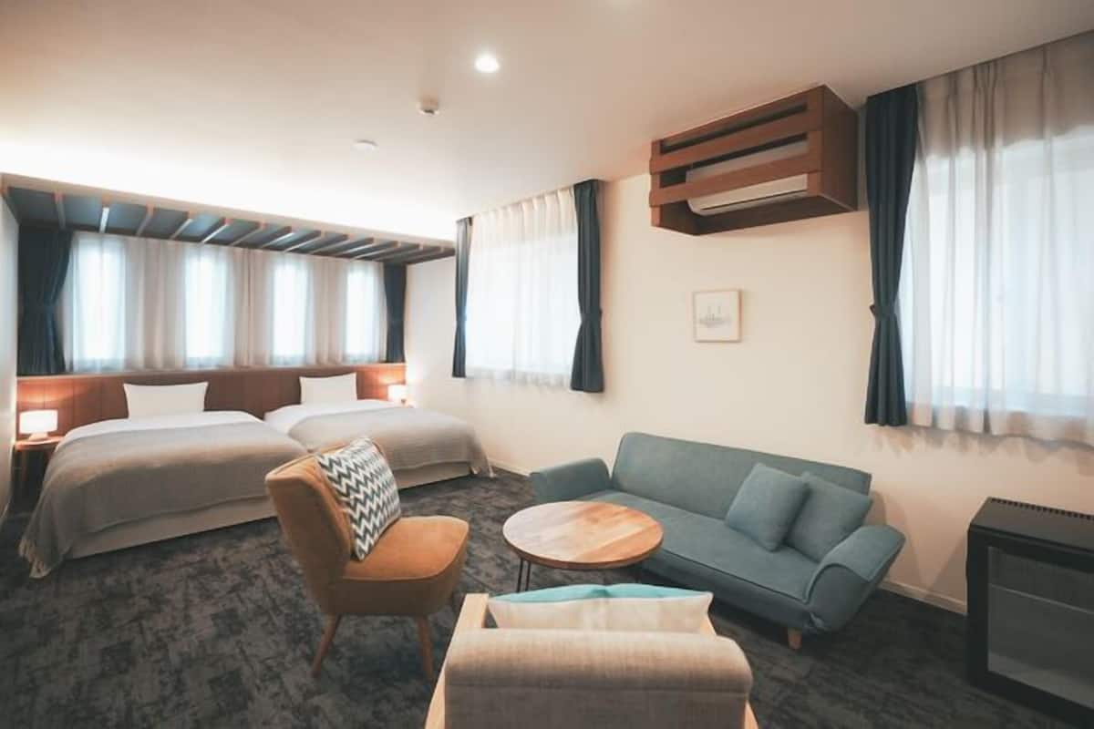 Habitación de hotel con dos camas, un sofá, una silla, una mesita y una chimenea.