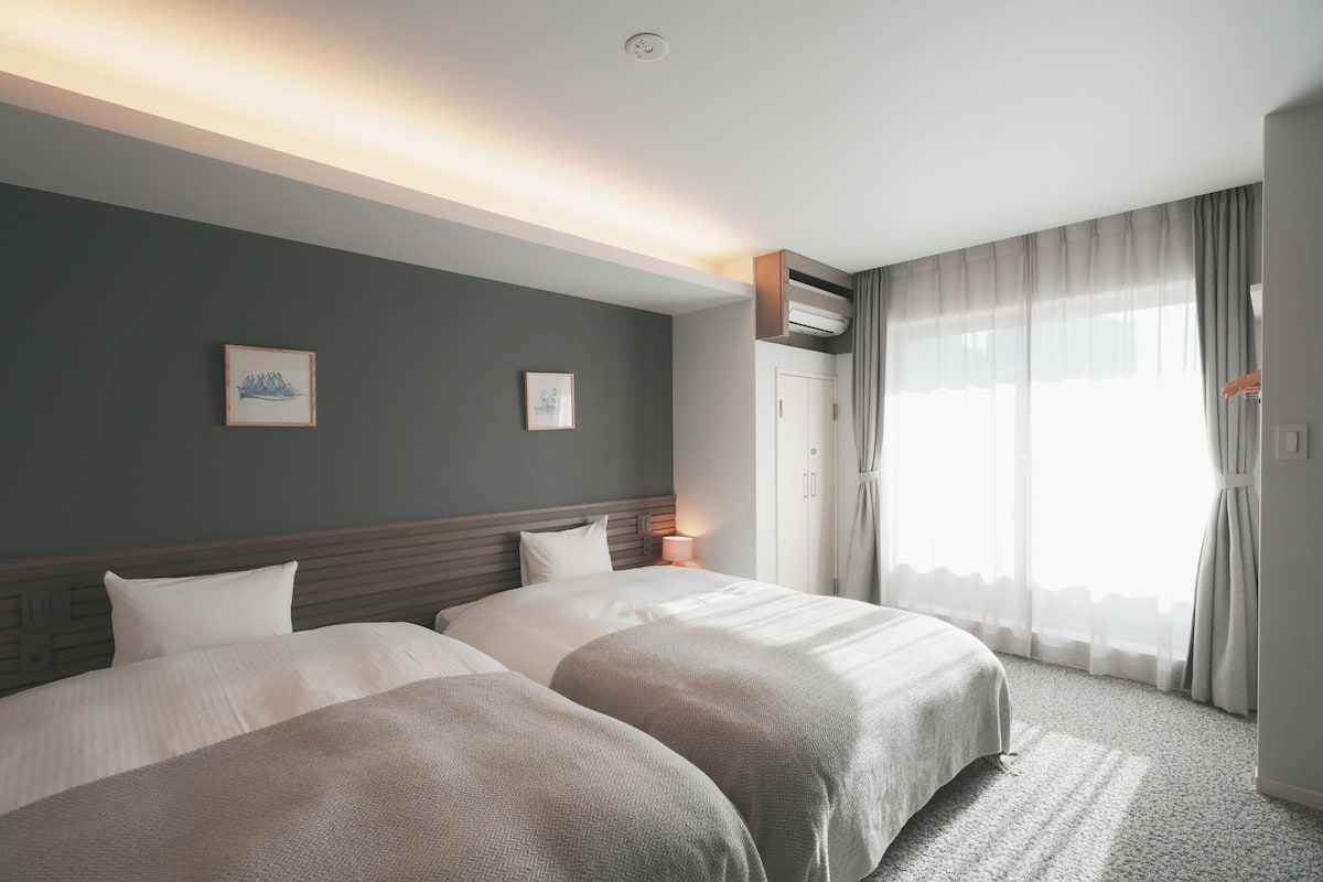 Une chambre d’hôtel avec deux lits, un luminaire au plafond, une fenêtre avec des rideaux et un climatiseur fixé au mur.