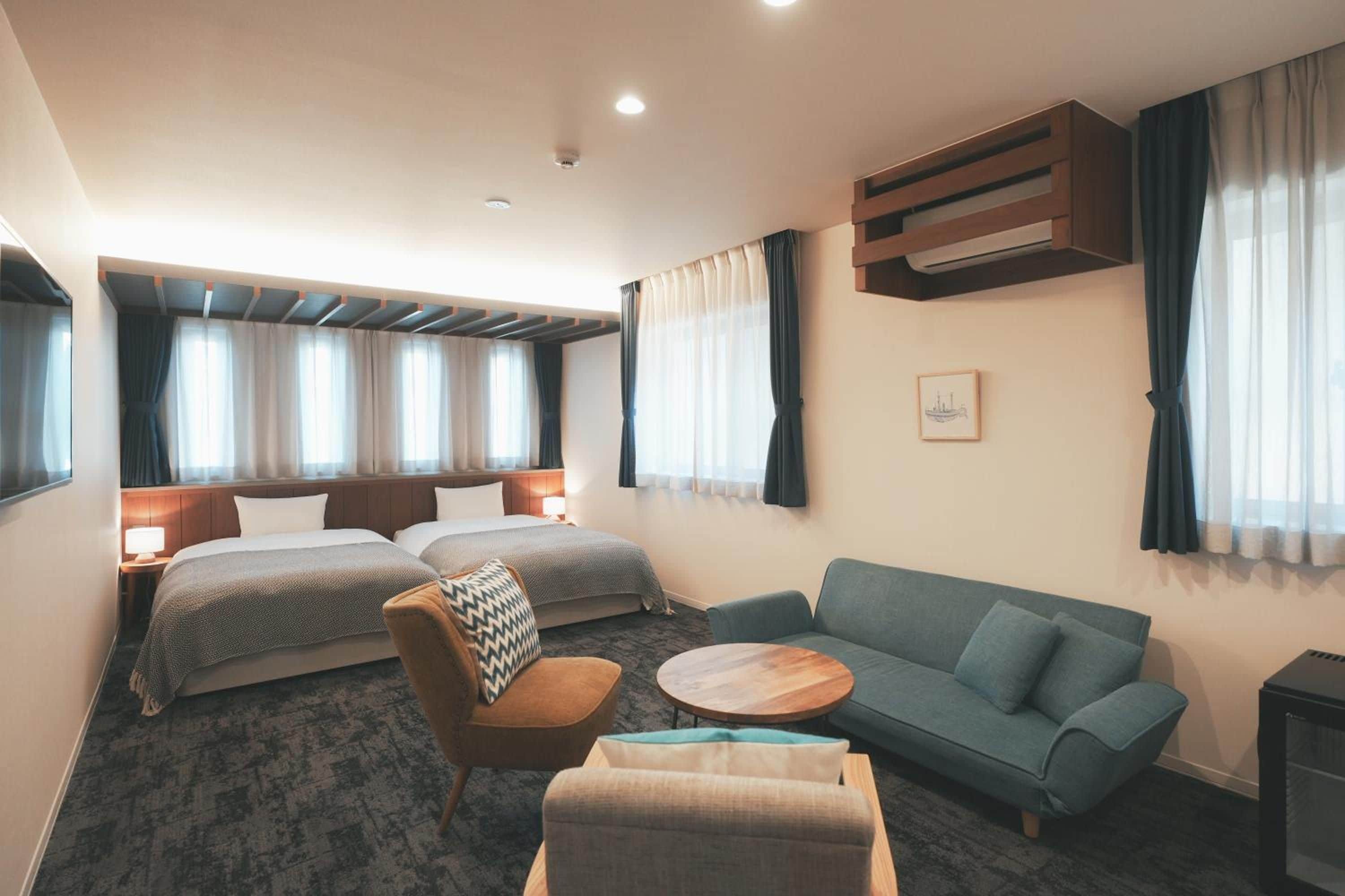 Une chambre d’hôtel avec deux lits, un canapé, une chaise, une petite table et un radiateur.