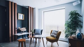 A modern living room with a large window, a sofa, a coffee table, and a small side table. - Lazuli Hiroshima Hotel & Lounge (Hiroshima)