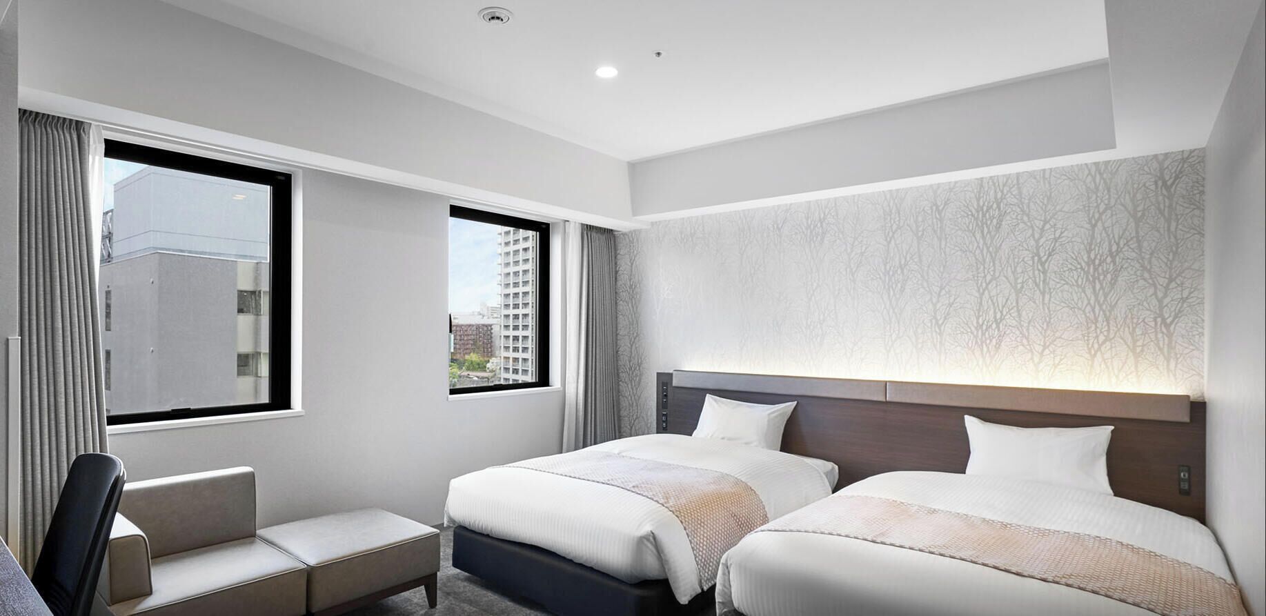 A hotel room with two beds, a seating area, and a large window with a view of buildings.