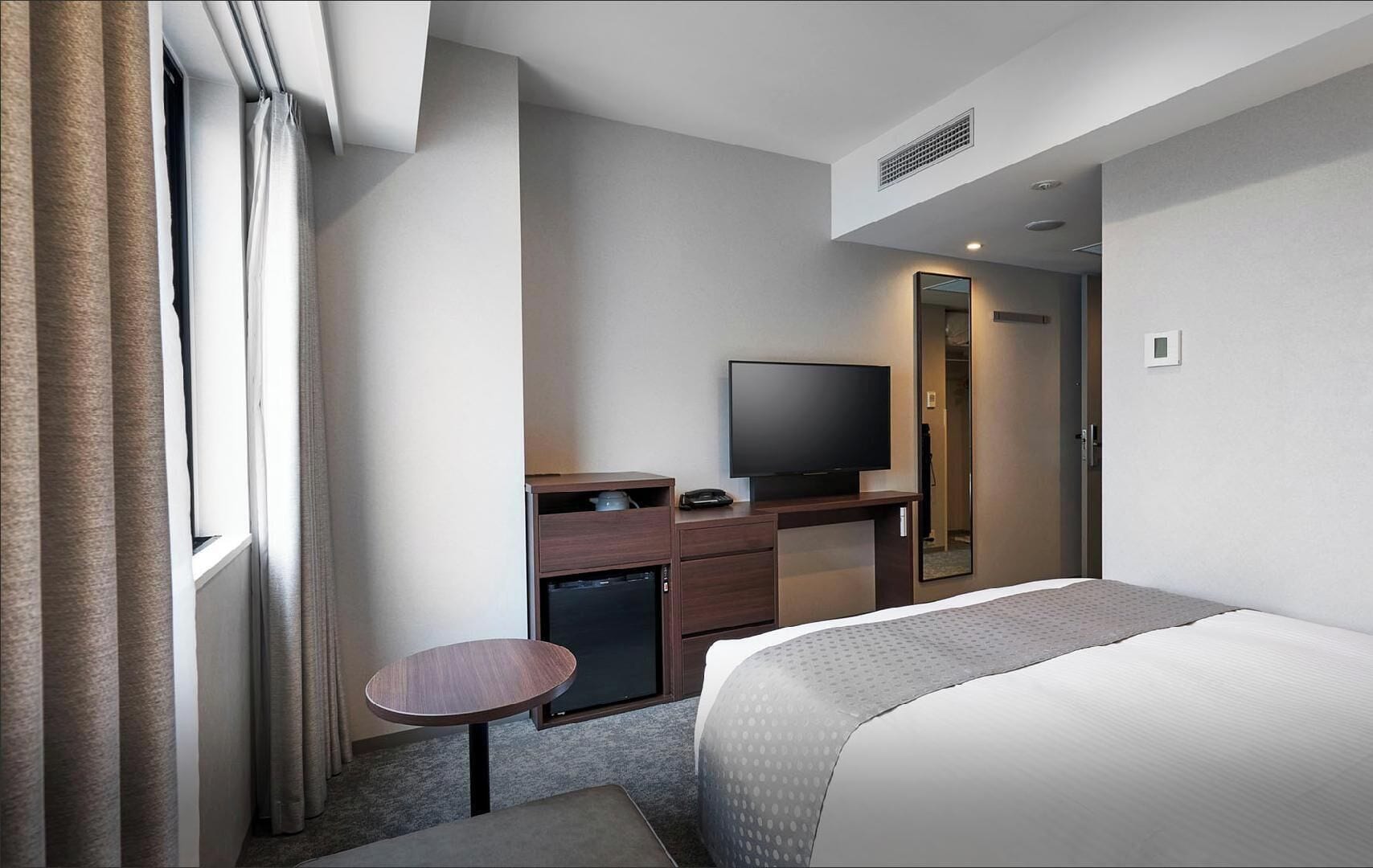 A hotel room with a bed, a desk with a television, a small table, and a wardrobe.