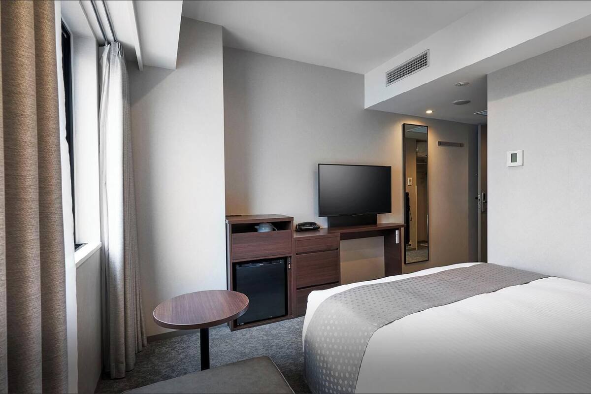 A hotel room with a bed, a desk with a television, a small table, and a wardrobe.