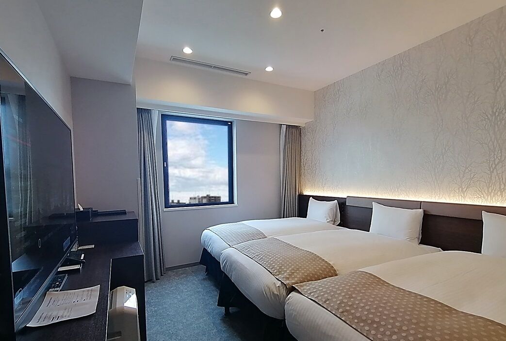 A hotel room with two beds, a TV, a desk, and a window with a view.