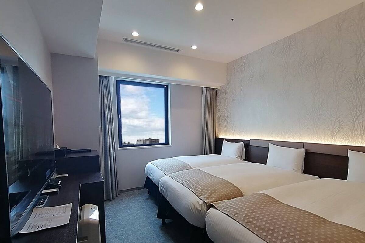A hotel room with two beds, a TV, a desk, and a window with a view.
