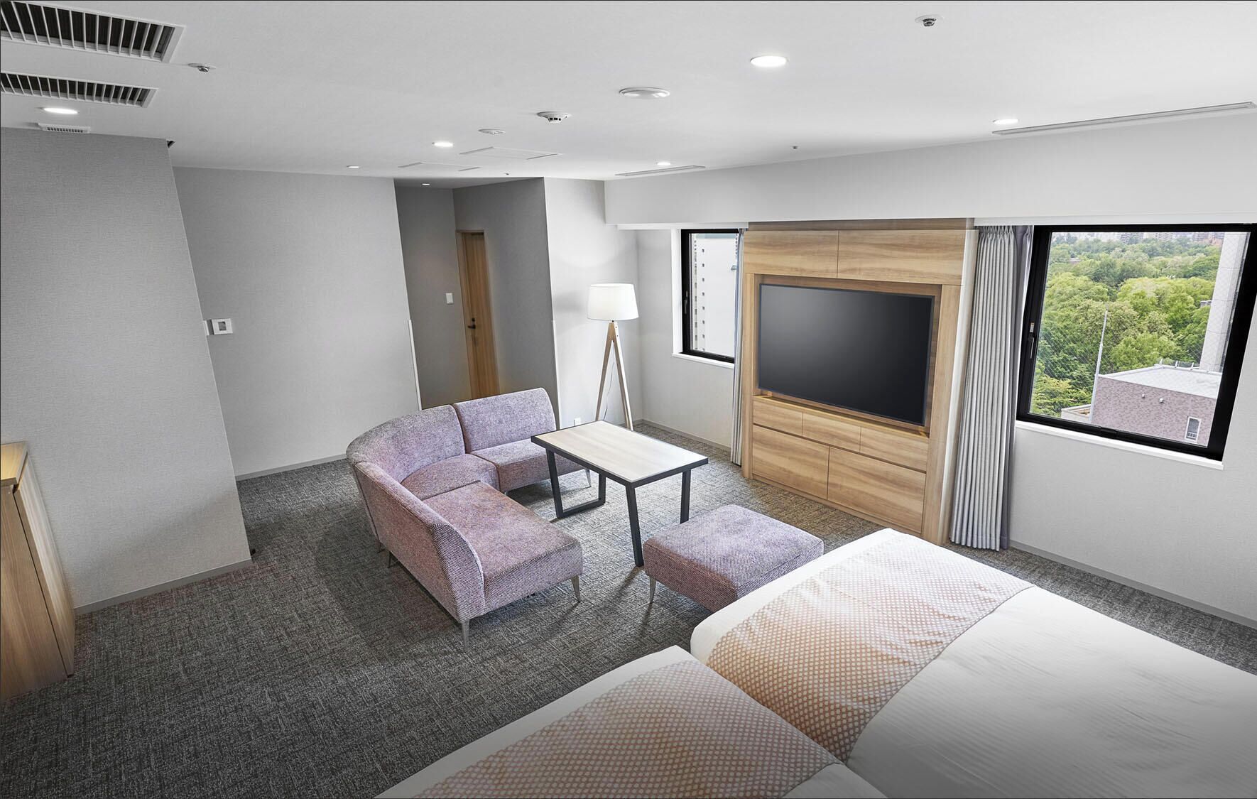 A hotel room with a bed, a sofa, a small table, a TV, and a window with a view.