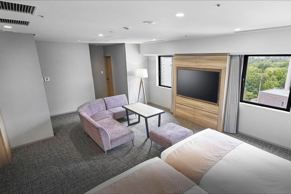 A hotel room with a bed, a sofa, a small table, a TV, and a window with a view.