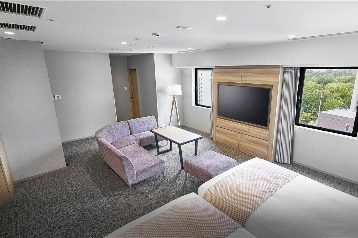 A hotel room with a bed, a sofa, a small table, a TV, and a window with a view.
