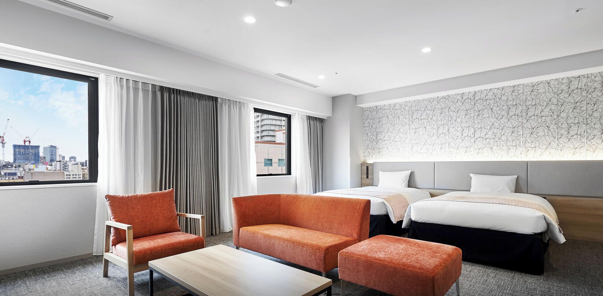 A hotel room with two beds, a sofa, a chair, a table, and a city view.