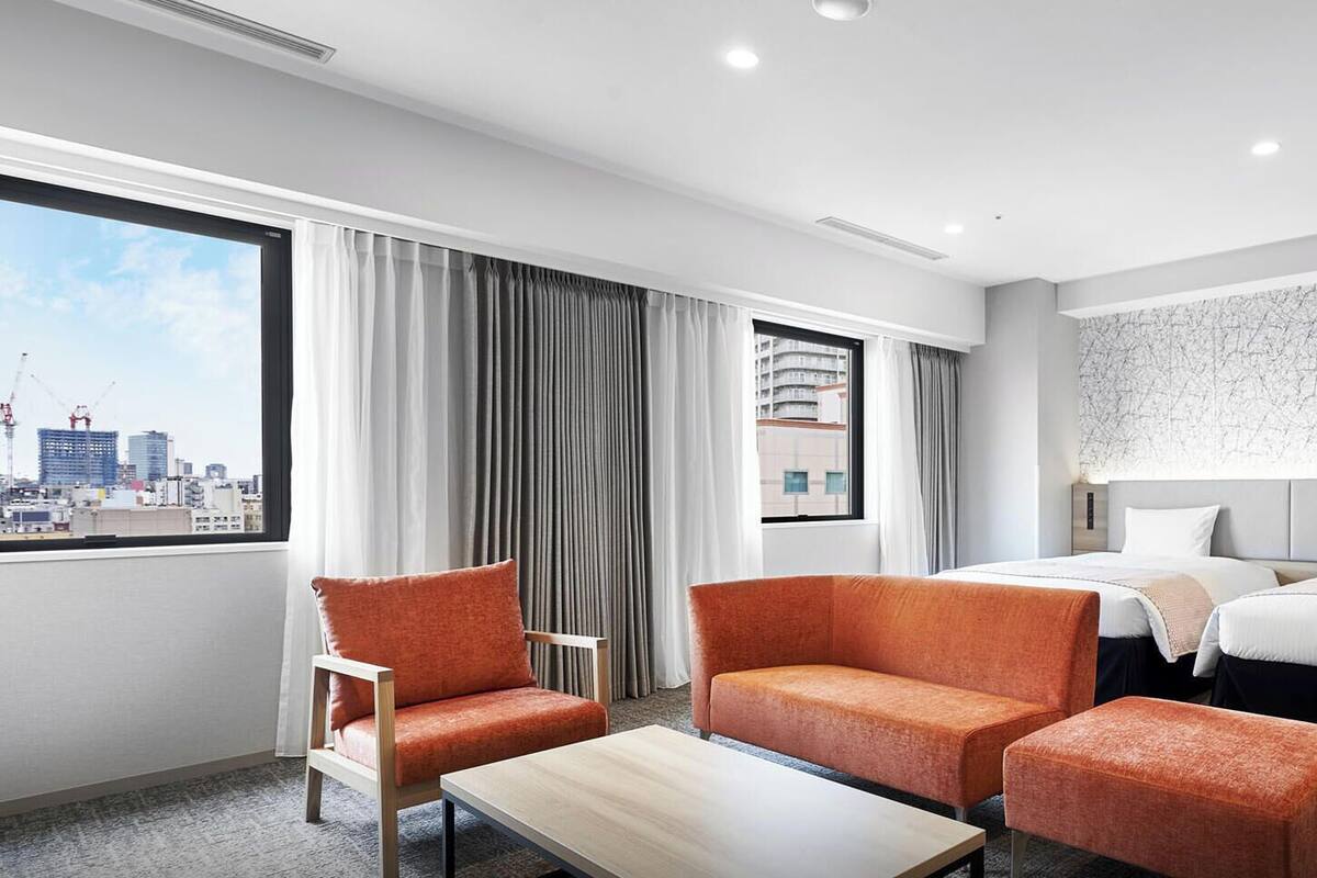 A hotel room with two beds, a sofa, a chair, a table, and a city view.