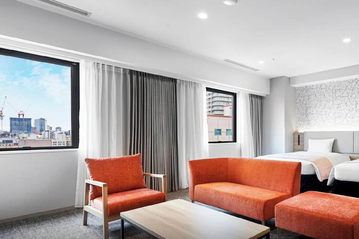 A hotel room with a city view, two beds, a sofa, a coffee table, and a patterned wall.