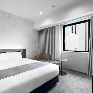 Une chambre d’hôtel moderne avec un grand lit, un petit coin salon, une table ronde et une fenêtre avec des rideaux.