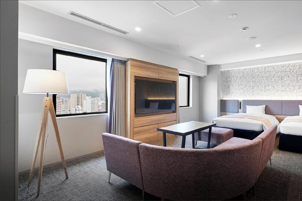 A hotel room with a city view, a sofa, a small table, a TV, and a bed.