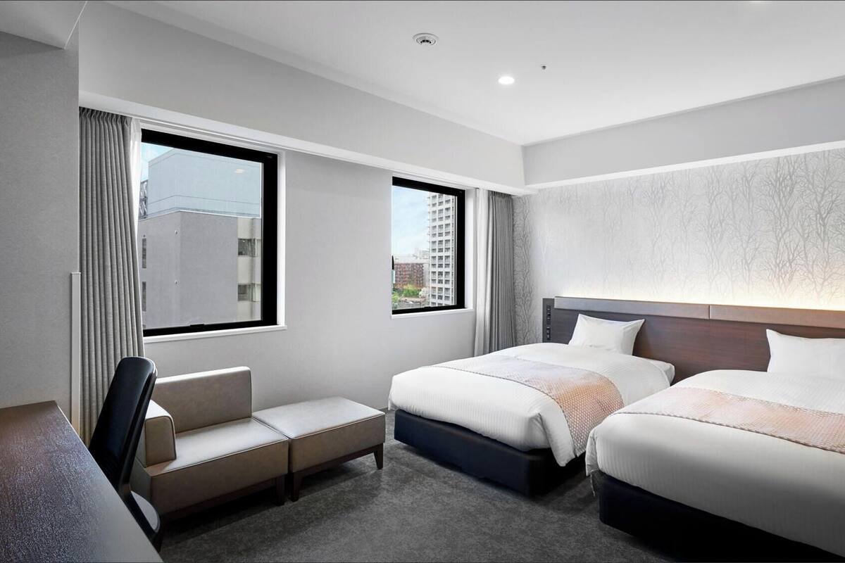 A hotel room with two beds, a desk, and a chair.