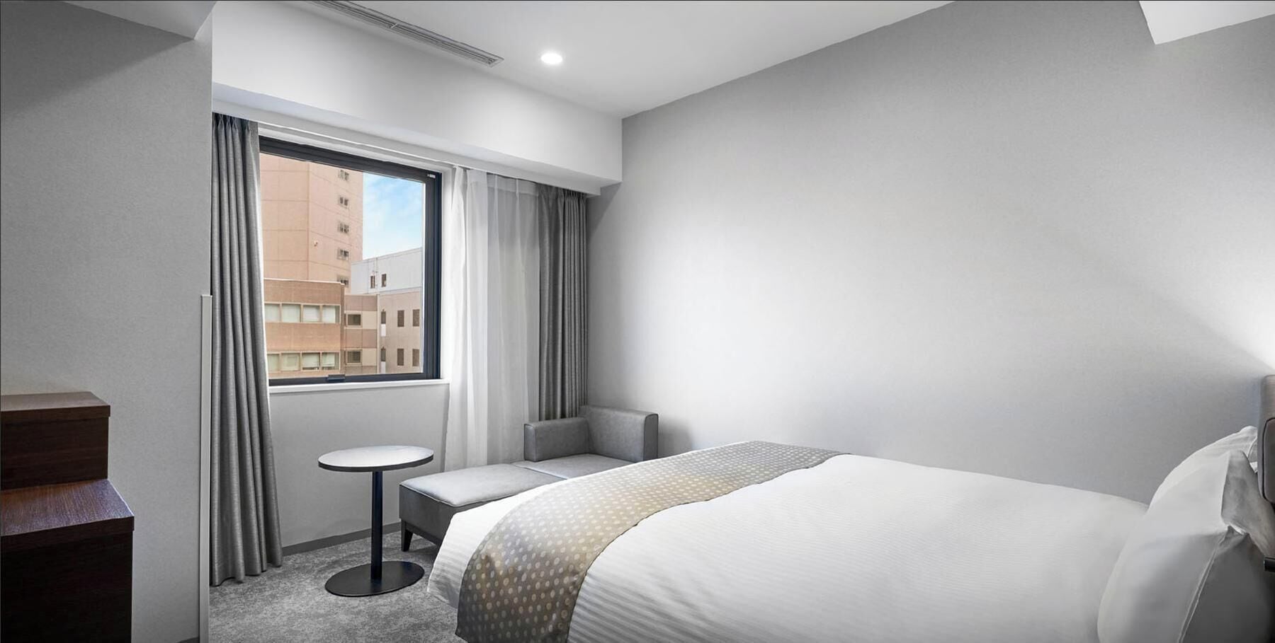 A hotel room with a large bed, a small round table, a chair, a desk, and a window with curtains.