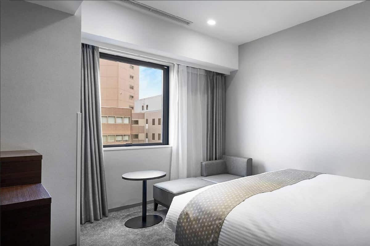 A hotel room with a large bed, a small round table, a chair, a desk, and a window with curtains.