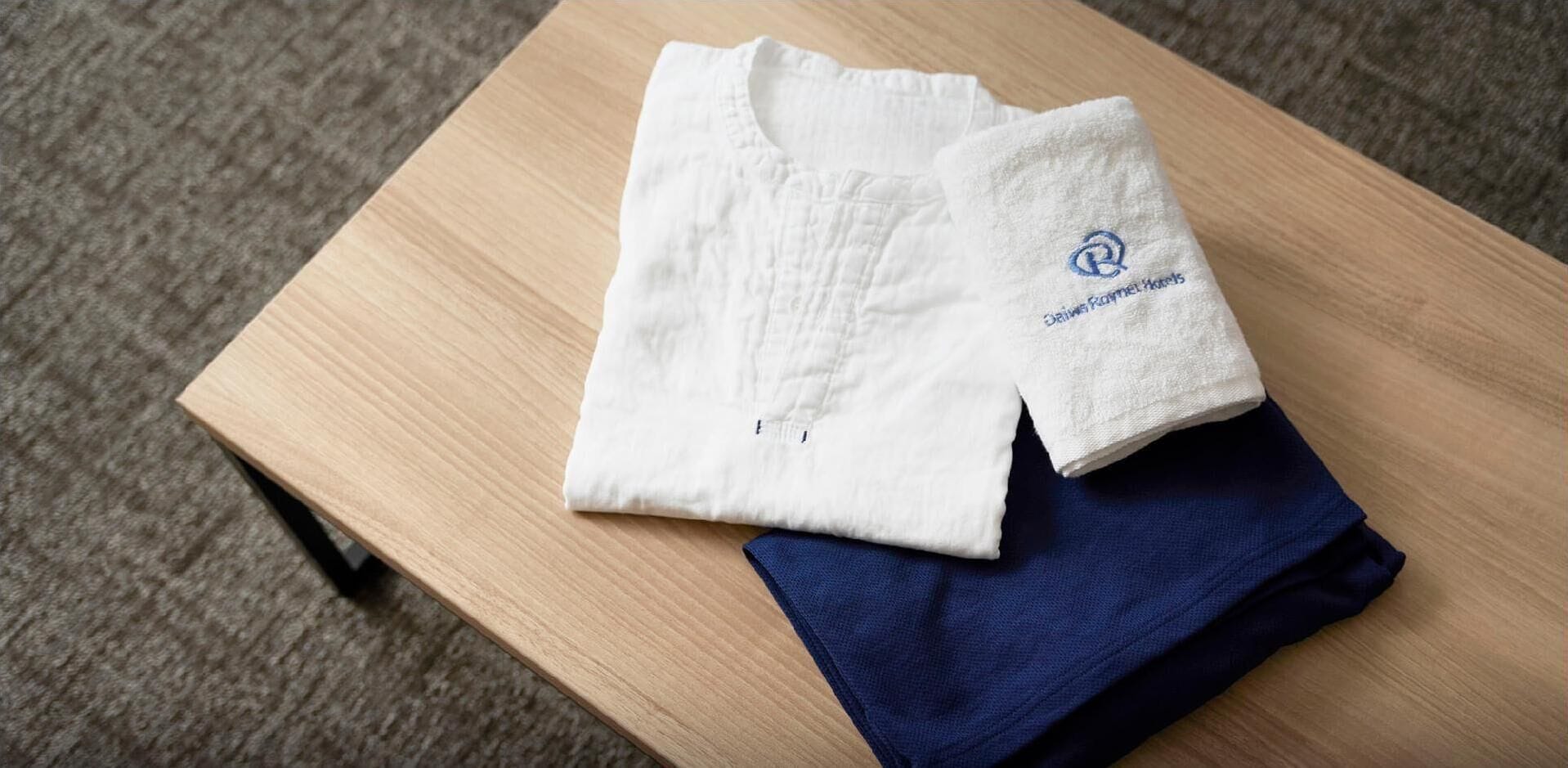 Ein weißes Hemd mit einem Logo und ein gefaltetes blaues Kleidungsstück auf einer Holztisch.