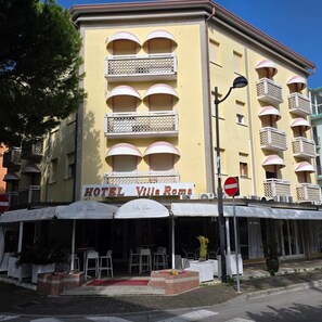 Un hotel con fachada amarilla, varios balcones y mesas al aire libre.