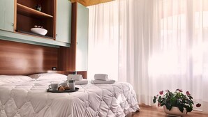 A hotel room with a bed, a breakfast tray, a vase with flowers, and a window with curtains. - Villa Roma (Caorle)