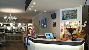 A modern reception area with a curved counter, a chandelier, and a large painting on the wall. - Villa Roma (Caorle)