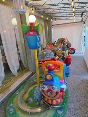 Un paseo infantil colorido con una estructura tipo tren y un carruaje tirado por caballos al fondo.
