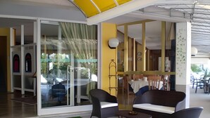 A modern interior with a green carpet, a glass door entrance, and a dining area with tables and chairs. - Villa Roma (Caorle)