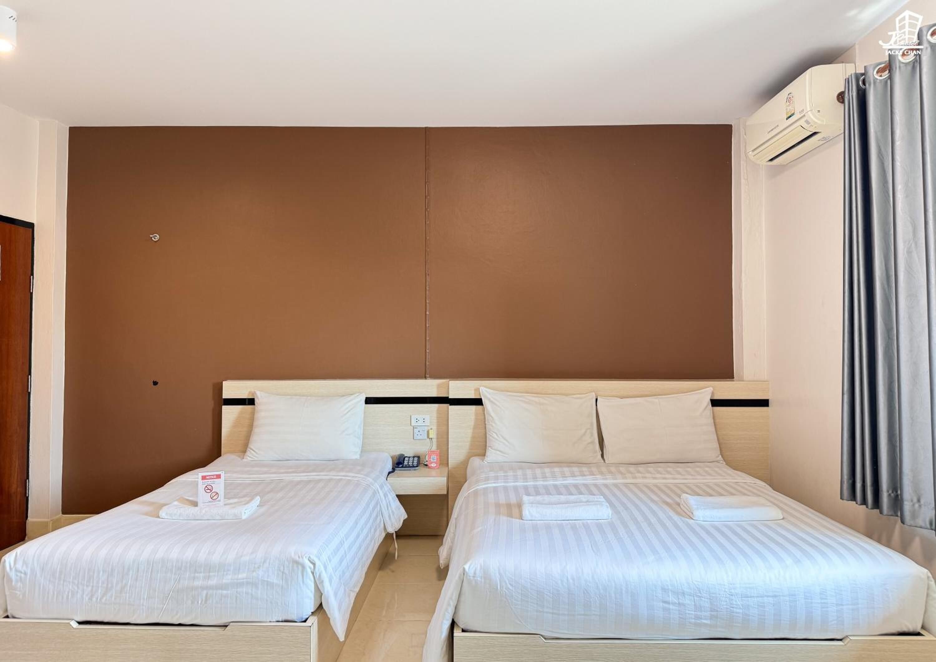 Ein Hotelzimmer mit zwei Einzelbetten, einem Holzkopfstück, einer Wand in Braun und einem Fenster mit Vorhängen.