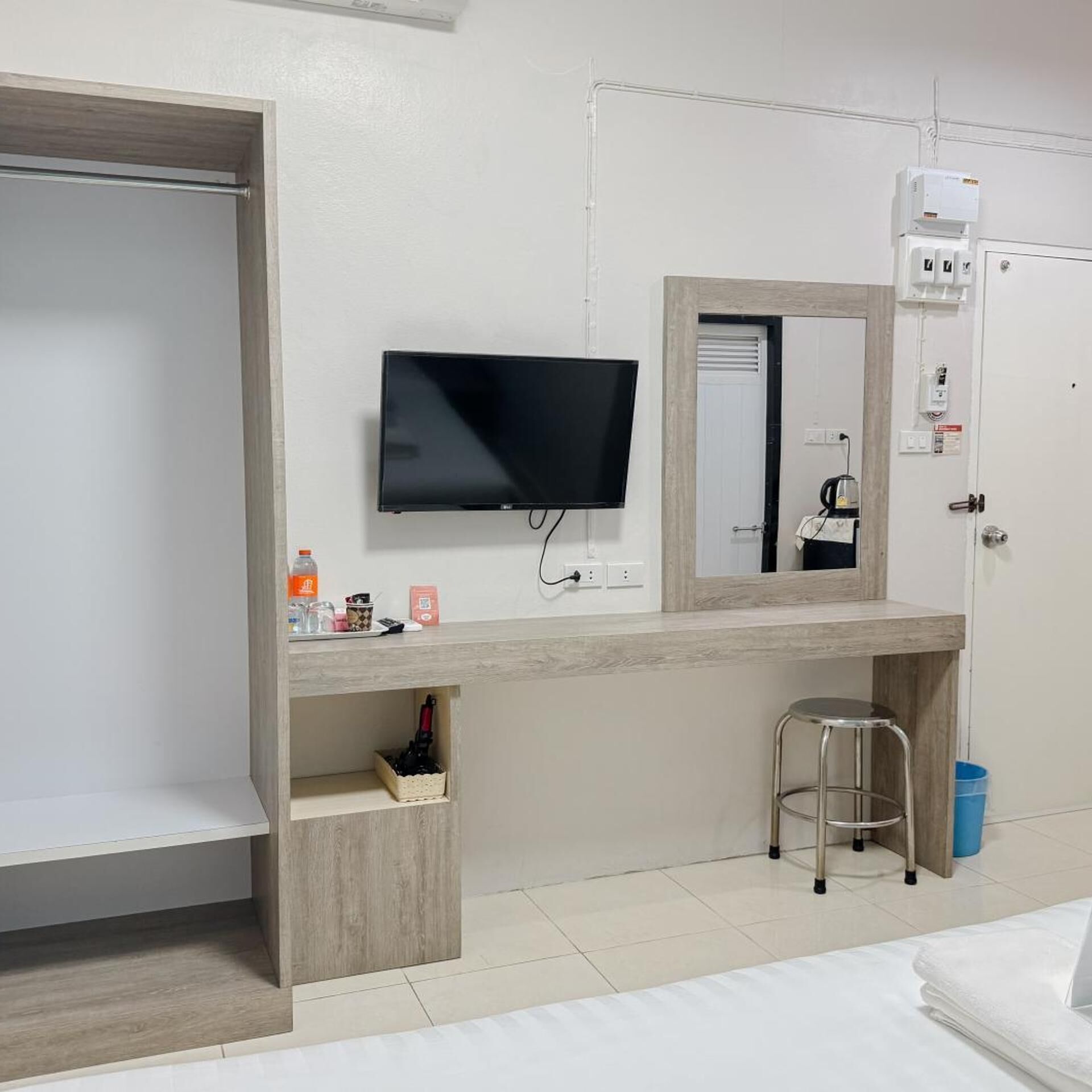 Ein Hotelzimmer mit Fernseher, Spiegel, Schreibtisch aus Holz, einem kleinen Hocker und einem Kleiderschrank.