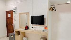 A room with a wooden door, a mirror, a flat-screen TV, a kettle, a small fridge, a trash bin, and a stool. - Jacky Chan Hotel (Betong)