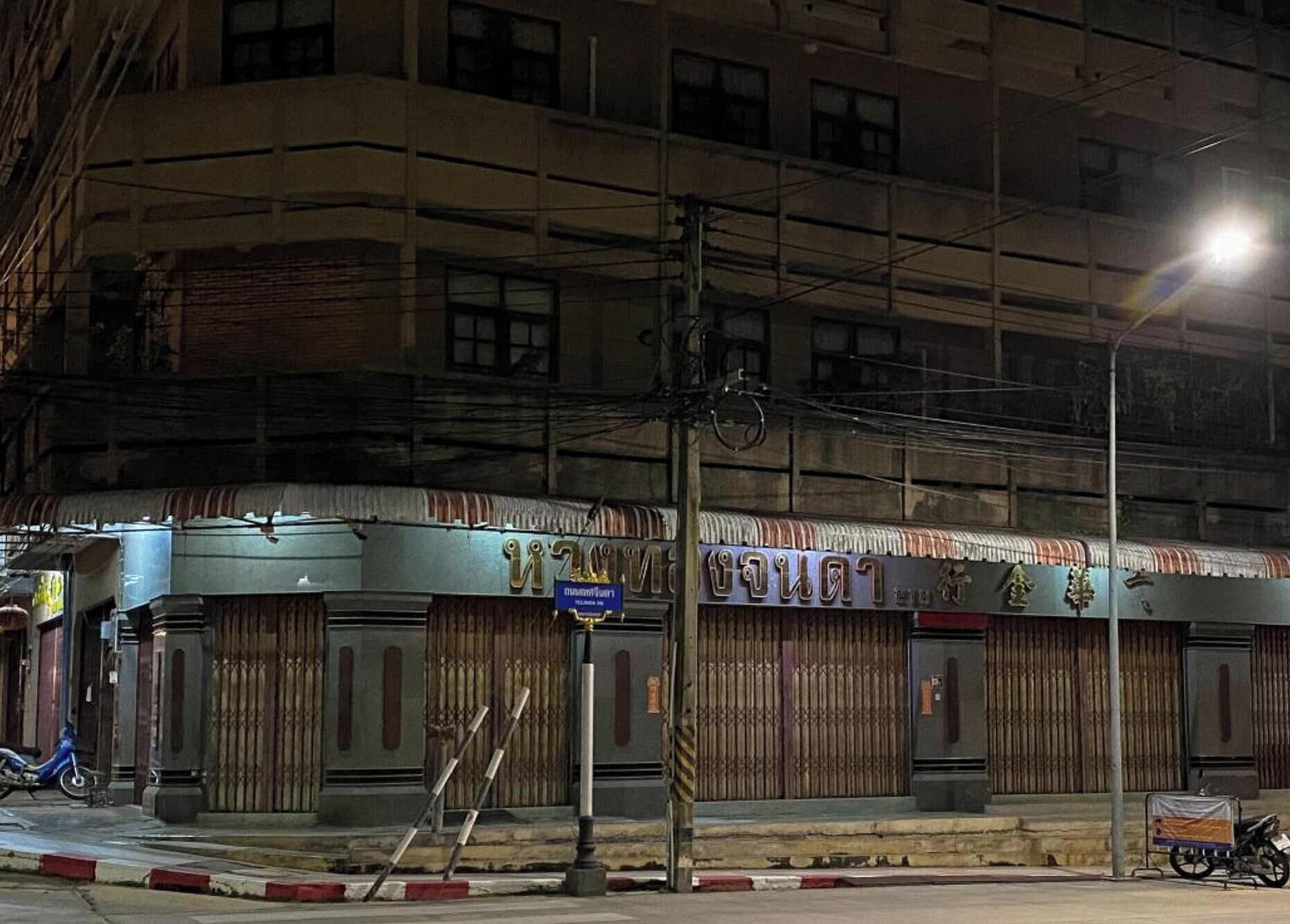 Een gebouw met verschillende gesloten winkelruiten, een zichtbare straatlamp en een geparkeerde motor.