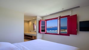 A hotel room with a bed, a large window with red shutters, a TV mounted on the wall, and a view of the sea. - 11:11 By Potnia Theron - Adults Only (Santorini)