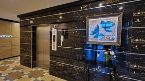 A modern hotel lobby with a check-in counter, an elevator, and a hallway with doors.
