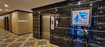 Un moderno vestíbulo de hotel con mostrador de recepción, un ascensor y un pasillo con puertas.