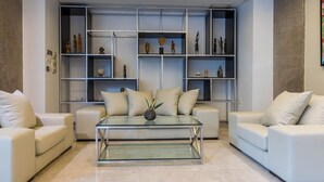 A modern living room with a glass coffee table, white sofas, and a built-in shelving unit with decorative items. - Boho Boutique Hotel Amman (Amman)
