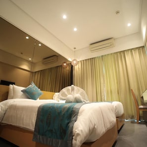 A modern hotel room with a large bed, a bedside table, an air conditioning unit, and a view of the outside through sheer curtains. - The Byke Delotel, Borivali (Mumbai)