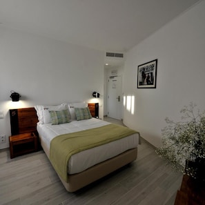 Quarto com cama, mesas de cabeceira, luminária na parede, quadro emoldurado e planta em vaso.