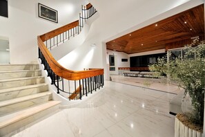 Un interior moderno con una escalera curva, suelo de mármol, techo de madera y una zona de estar con una planta en maceta.