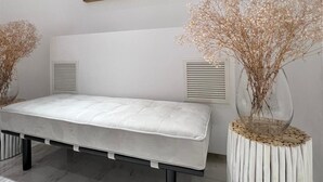 A minimalist room with a white bench, a framed painting, and two decorative vases with dried flowers. - Hotel Buzio (Sines)